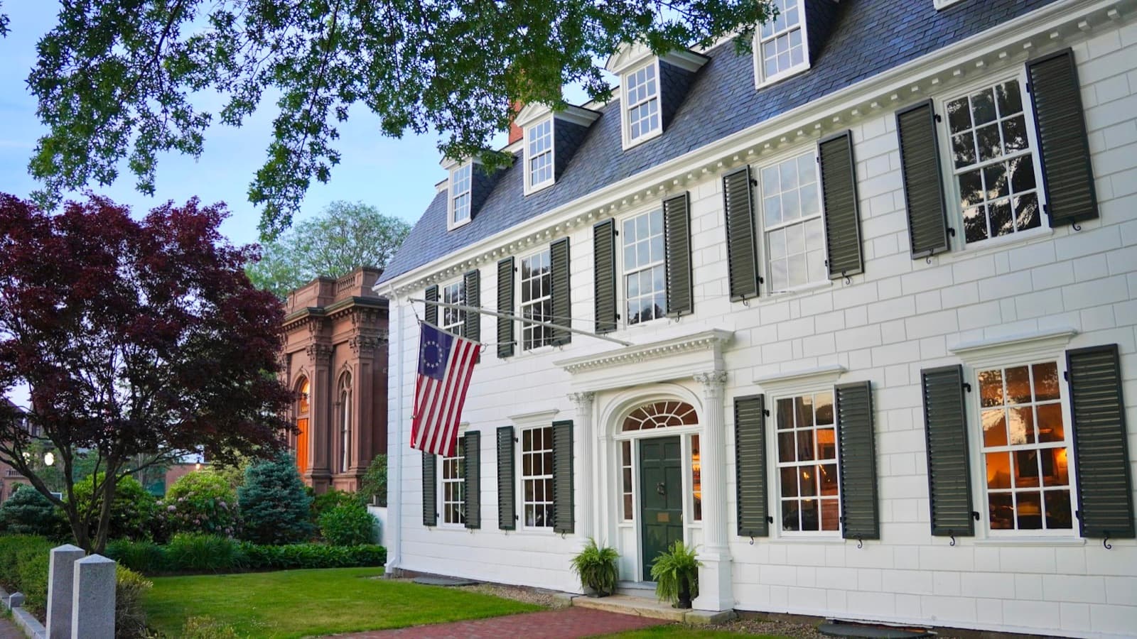 A white colonial home at dusk, lights on